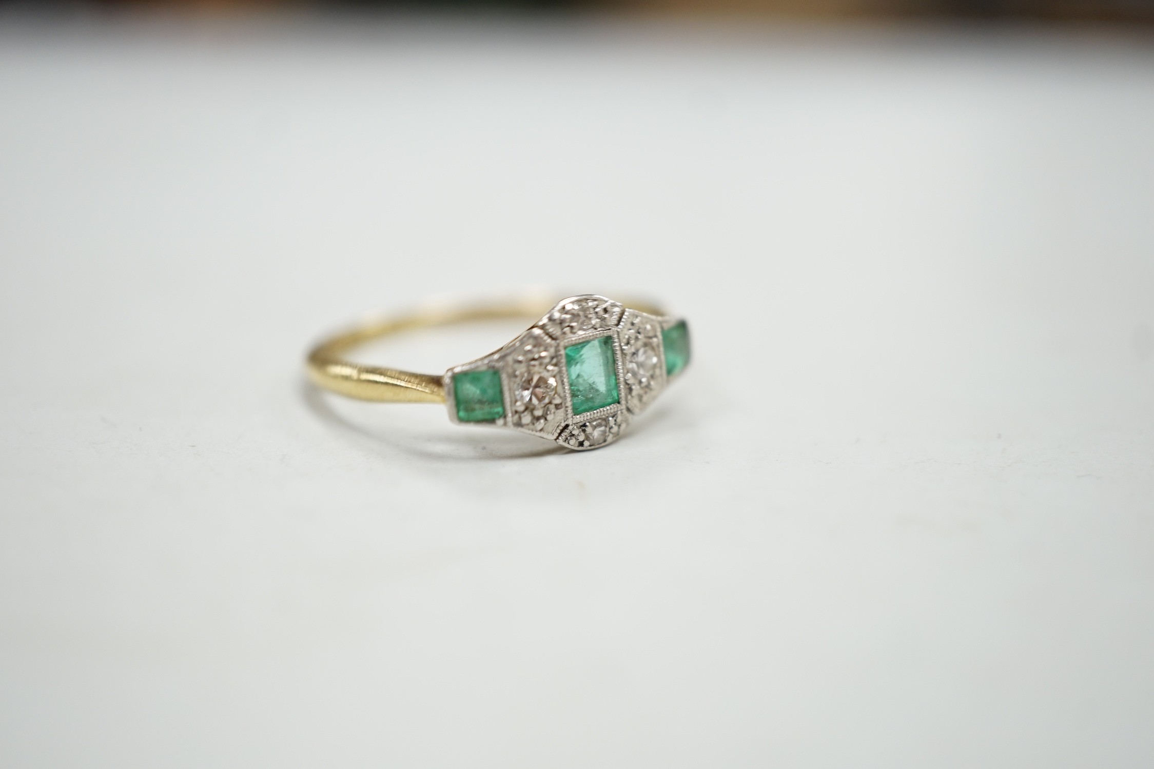 A 1920's 18ct & plat, millegrain set three stone emerald and four stone diamond ring, size R/S, gross weight 2.5 grams.